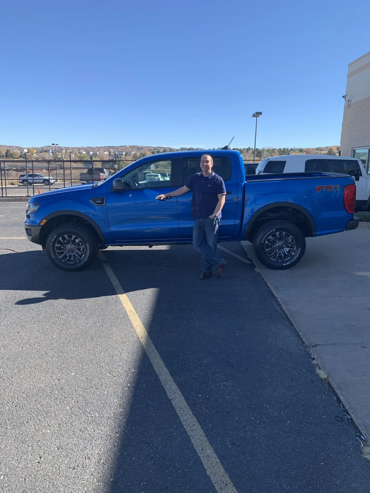A man is next to a blue Ford Ranger, highlighting CarVault Consulting's automotive expertise.
